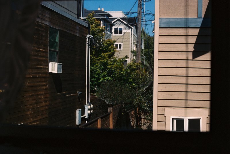 Sunlight and shadow fall across two houses and the narrow space between them.