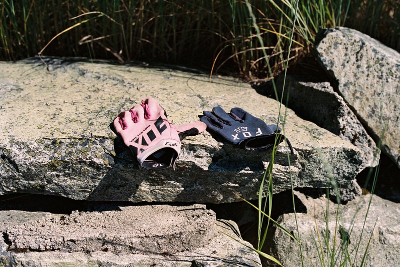 Pink and dark blue cycling gloves lie on a sunlit stone wall.