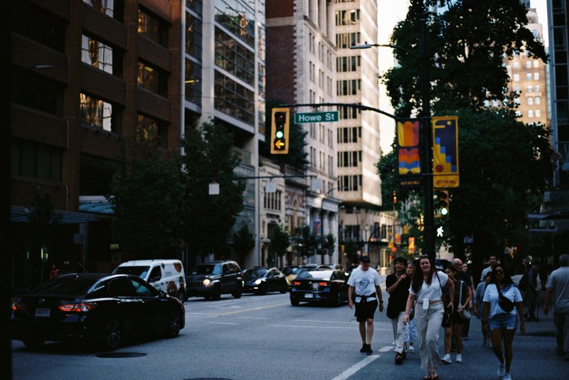Pedestrians cross a busy street beneath the Howe Street sign.